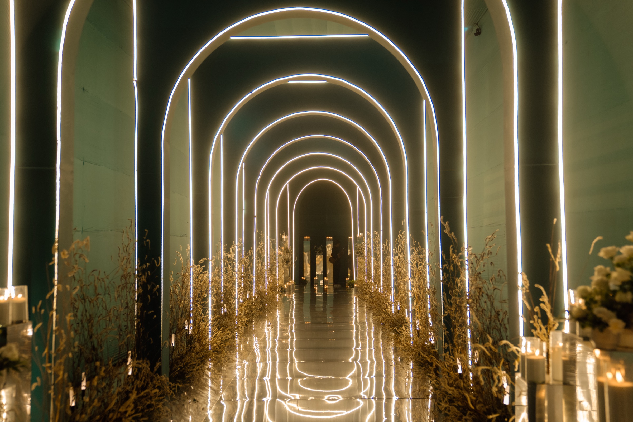 Tunnel of glowing white arches lined with golden grasses and candles, the entrance to the Sufiyana Shaam evening