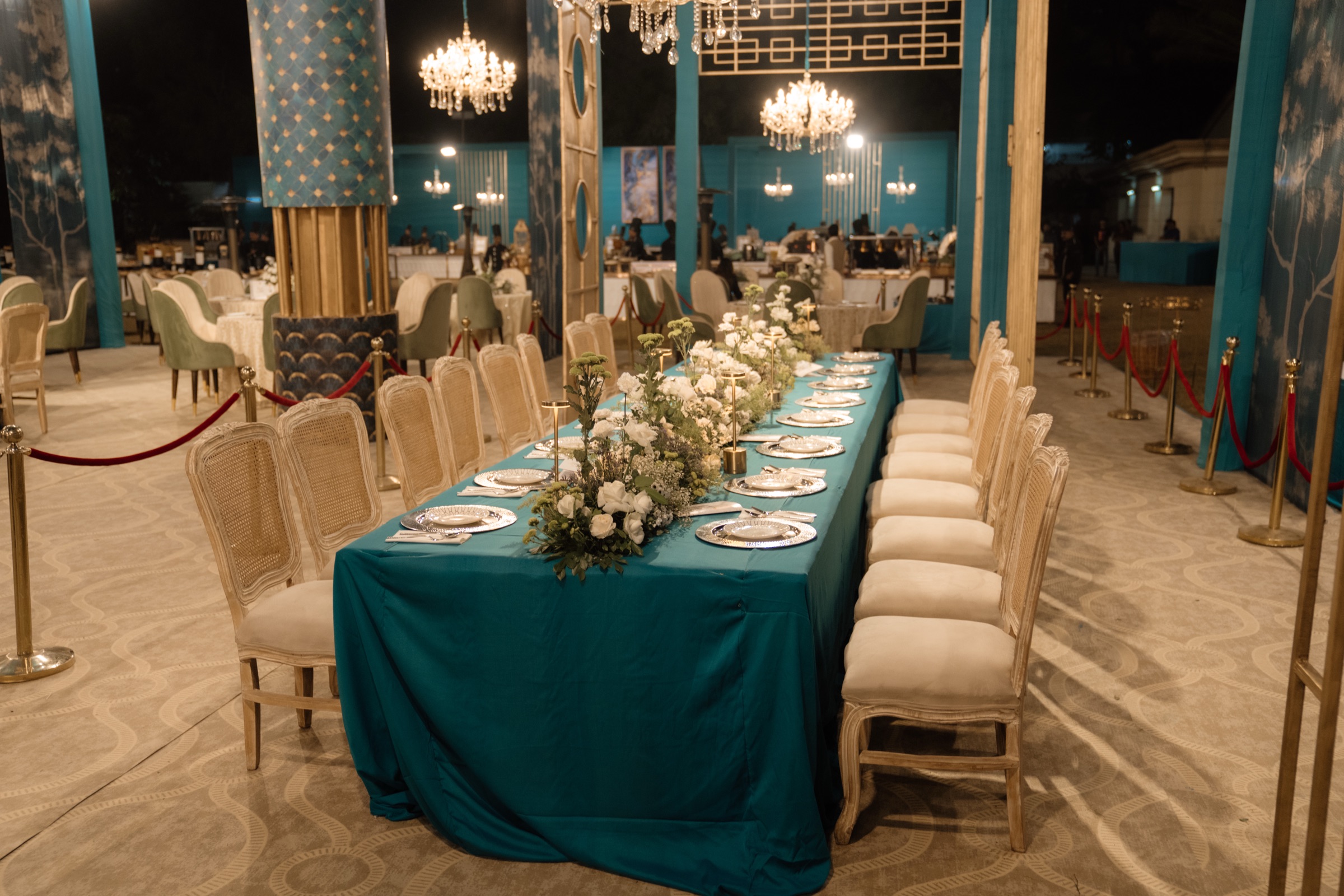 Teal and gold dining area with a white floral runner and crystal chandeliers